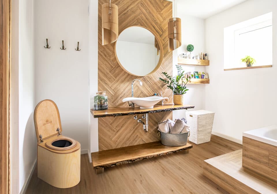Weißes Waschbecken auf einer Holztheke mit einem darüber hängenden runden Spiegel. Innenraum eines Badezimmers.
