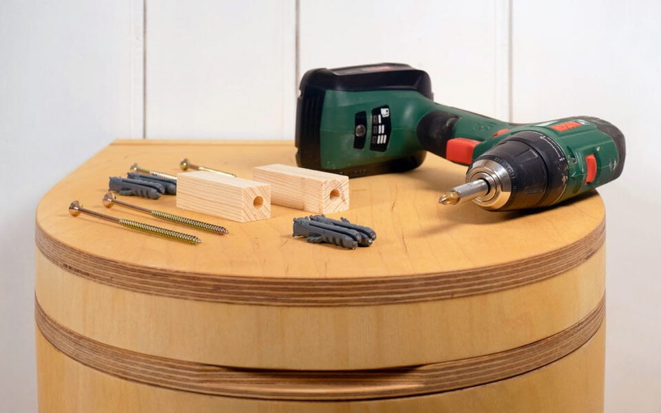 Werkzeug zum Trenntoilette selber bauen liegt auf dem Holzdeckel einer TROBOLO Trenntoilette