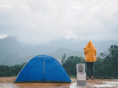 Campingtoilette TROBOLO WandaGO neben Zelt und Frau bei schlechtem Wetter