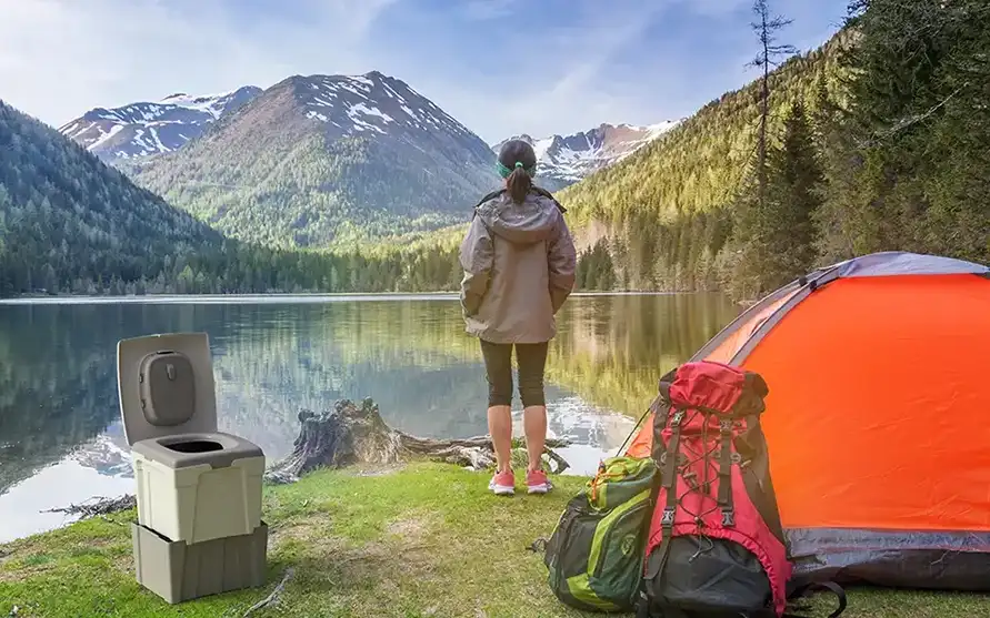 Toilette compostante TROBOLO WandaGO all'aperto nella natura con una donna davanti a una tenda e alle montagne