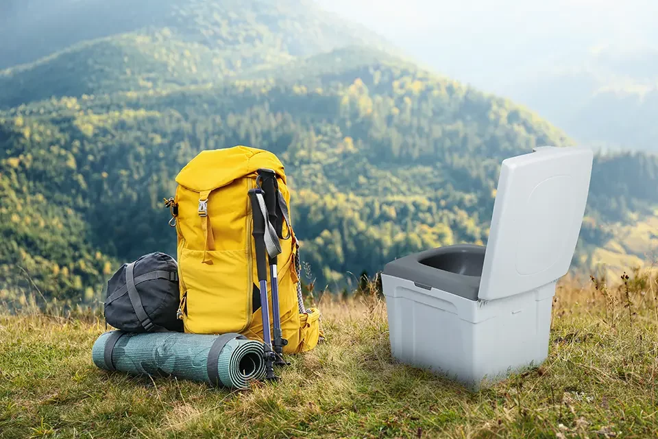 The WandaGO Lite composting toilet stands next to a backpacker overlooking the mountains.